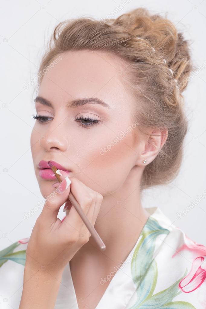 Makeup artist applies lipstick. Beautiful woman face. 