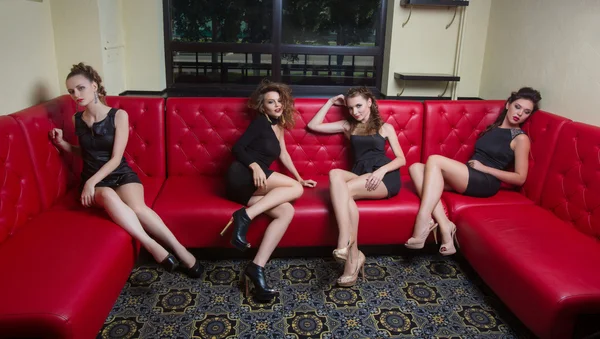 Quatre filles en robe courte noire sur un canapé rouge — Photo