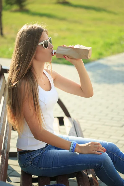 Fille boit d'une bouteille dans un sac en papier . — Photo