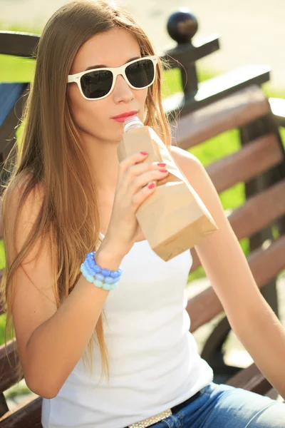 Chica bebe de una botella en una bolsa de papel . — Foto de Stock