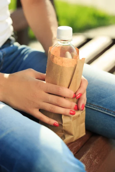 Girl holding a plastic bottle in a paper bag — Stock Photo, Image