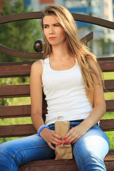 Chica bebe de una botella en una bolsa de papel . — Foto de Stock