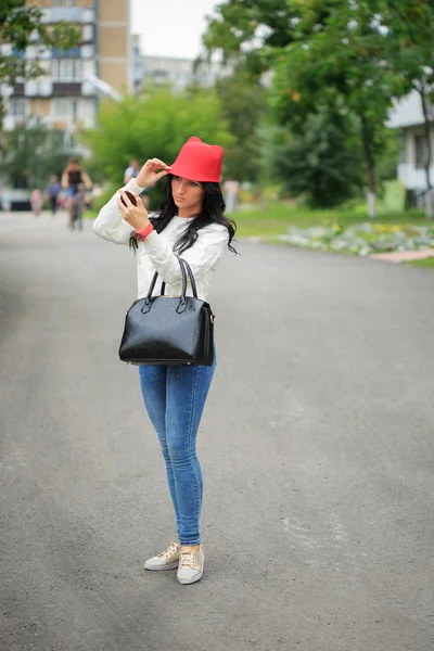 Дівчина в червоному капелюсі з вухами, тримає сумку на вулиці — стокове фото