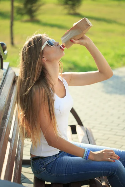 Girl drinks from a bottle in a paper bag. — Stock Photo, Image