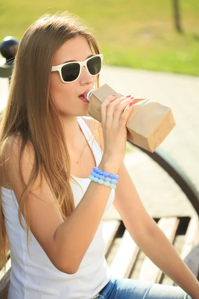 Girl drinks from a bottle in a paper bag. — Stock Photo, Image