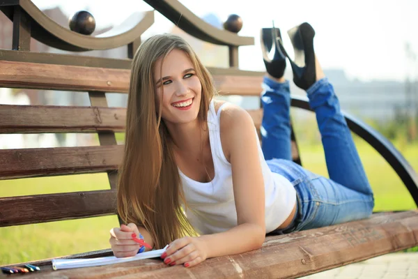 Young girl paints in a park sitting on a bench — Stock Photo, Image