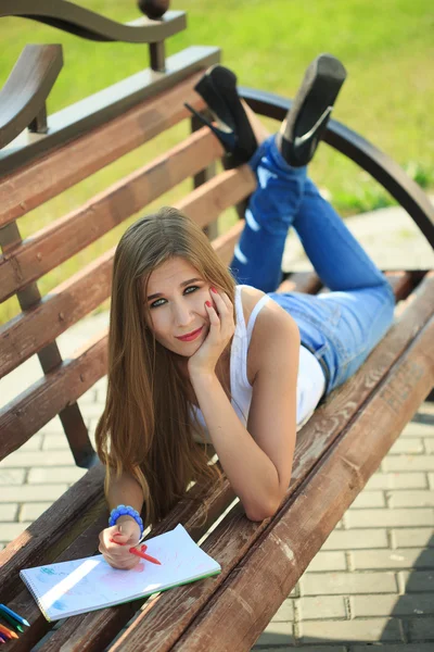 在公园的长椅上坐着的年轻女孩涂料 — 图库照片