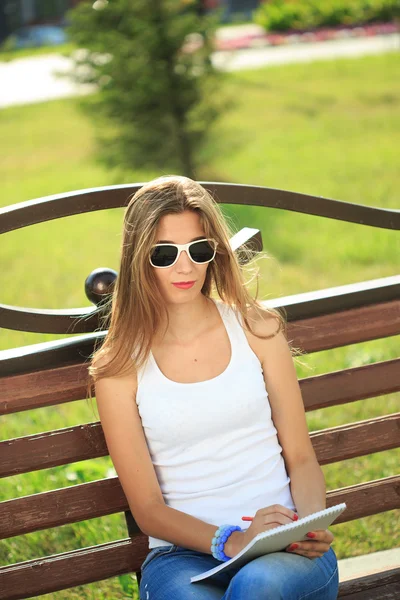 Jovem garota pinta em um parque sentado em um banco — Fotografia de Stock