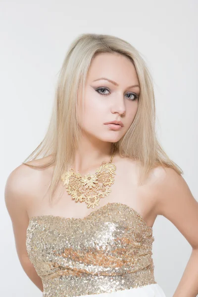 Schöne junge blonde Mädchen. in einer goldenen Kette und einem goldenen Kleid — Stockfoto