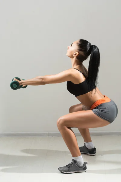 Ung, vacker, atletisk flicka utför knäböj med hantlar i ett gym. — Stockfoto