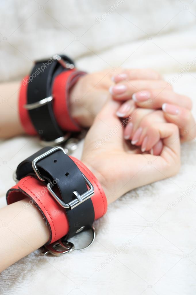 female hands in leather handcuffs. on the background sheet. sex toys.