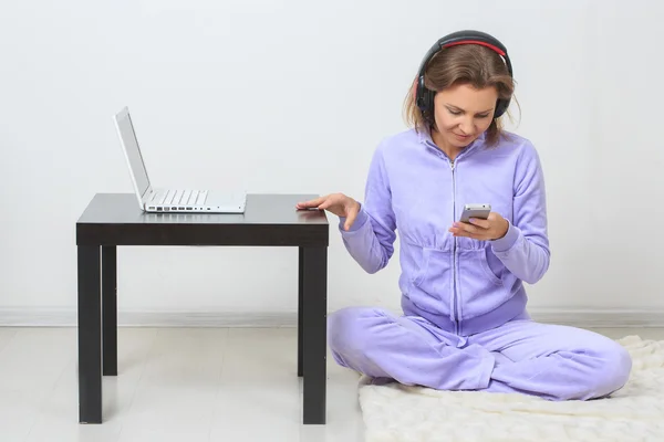Молодая женщина сидит на полу, слушая музыку с вашего телефона — стоковое фото