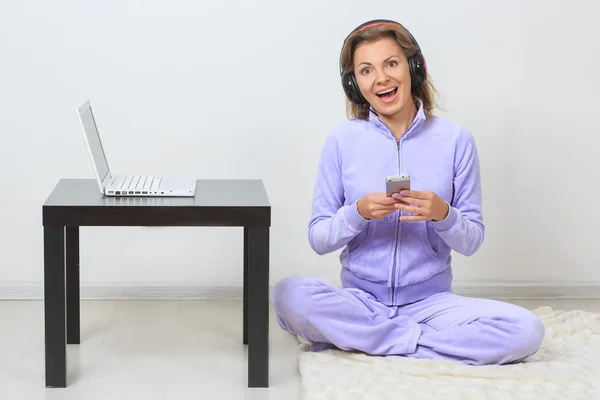 Mujer joven se sienta en el suelo, escuchando música desde su teléfono —  Fotos de Stock