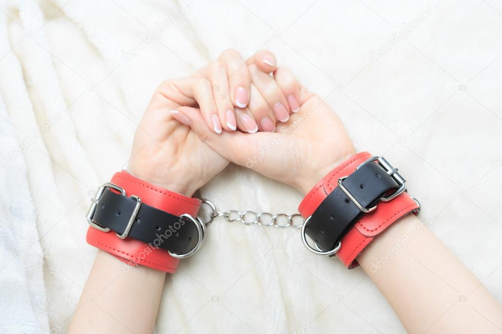 female hands in leather handcuffs. on the background sheet. sex toys.
