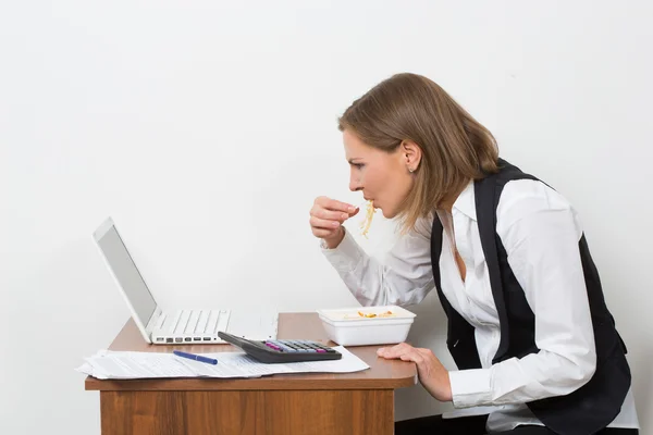 Chica come una pasta, trabajando detrás de la computadora portátil . — Foto de Stock