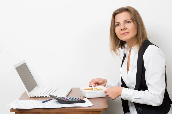 Дівчина їсть макарони, працює за ноутбуком . — стокове фото
