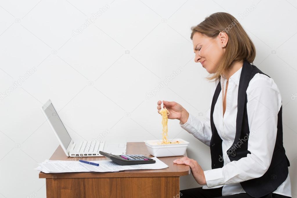 girl eats a pasta, working behind the laptop.