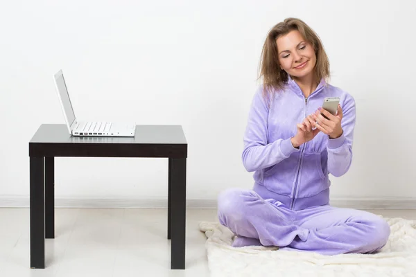 Menina alegre fala por telefone sentado em casa. próximo a um laptop — Fotografia de Stock