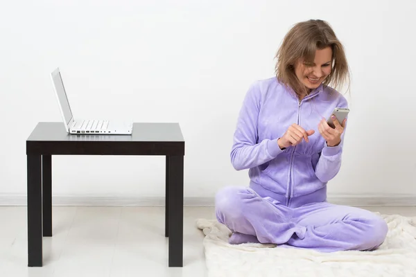 Neşeli kız telefonu evde oturarak konuşuyor. yanında bir dizüstü bilgisayar — Stok fotoğraf