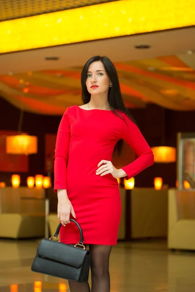 Beautiful young woman in a luxurious red dress posing with shopping bags — Zdjęcie stockowe