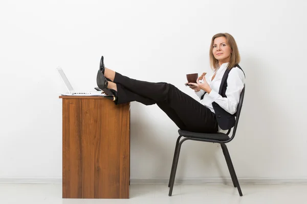 Девушка в офисе с ногами на столе и пьет кофе. шоколад — стоковое фото