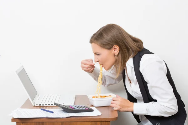 Fille mange une pâtes, travaillant derrière l'ordinateur portable . — Photo