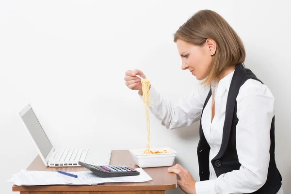 Gadis makan pasta, bekerja di belakang laptop . — Stok Foto