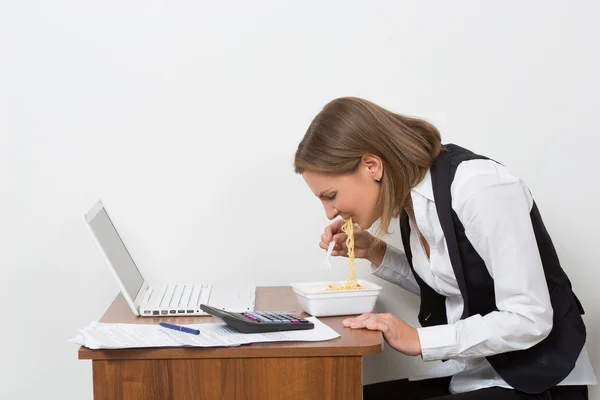 Tjej äter en pasta, arbetar bakom den bärbara datorn. — Stockfoto