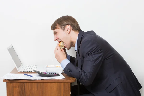 Uomo mangiare hamburger alla scrivania — Foto Stock