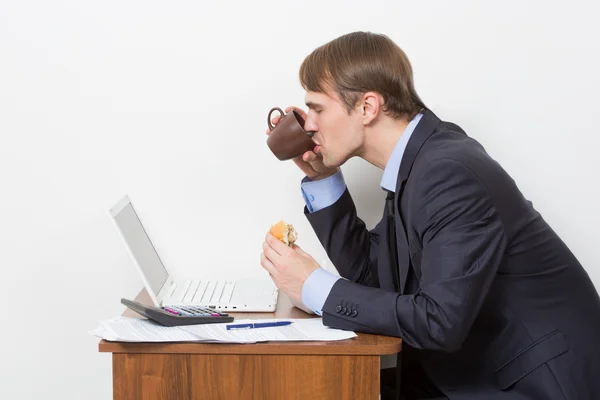 Homme mangeant un hamburger au bureau — Photo