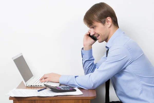 Man med en miniräknare vid sitt skrivbord på kontoret. talande telefon — Stockfoto