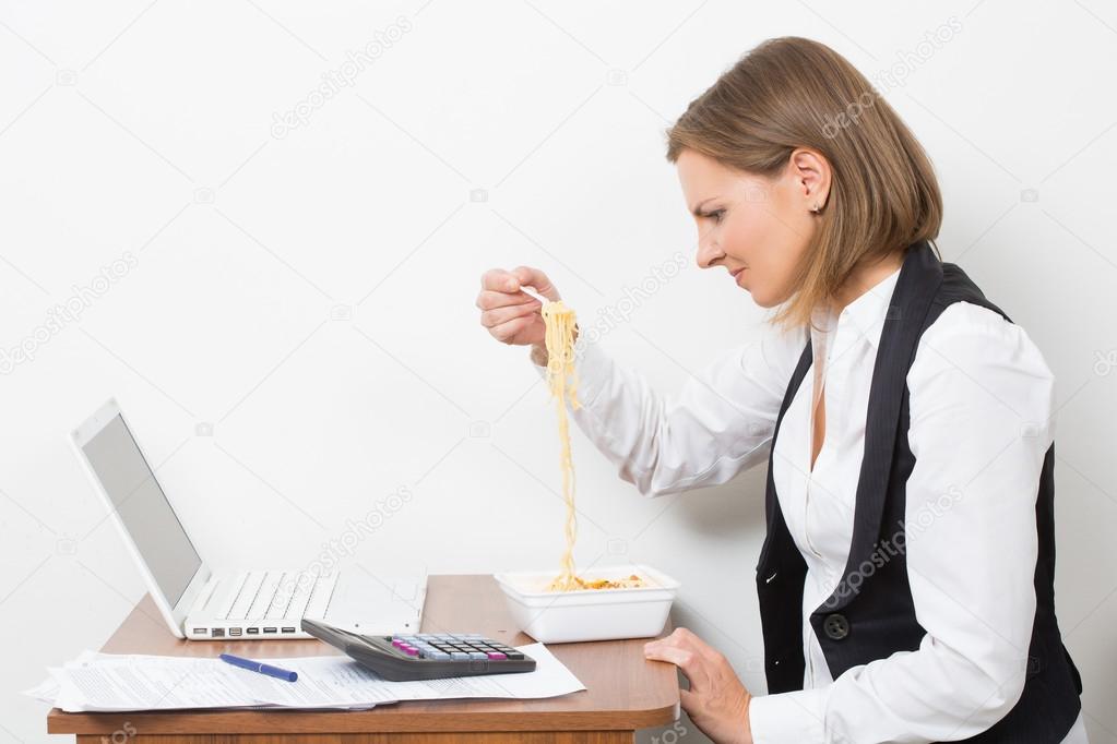 girl eats a pasta, working behind the laptop.