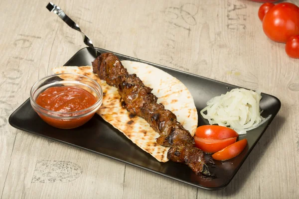 Saslik. kebab nyárs, fekete téglalap alakú lemez. mártással és hagymával — Stock Fotó