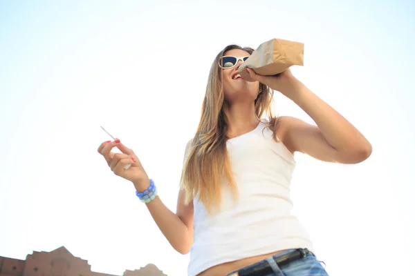 Meisje drinken uit een papieren zak in de straat. rookt. decadentie, anti-sociaal gedrag — Stockfoto