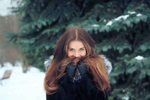 Belle fille souriante sur fond d'arbres enneigés. Portrait d'hiver. manteau avec capuche — Photo