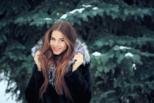 Hermosa chica sonriente en el fondo de los árboles nevados. Retrato de invierno. abrigo con capucha — Foto de Stock