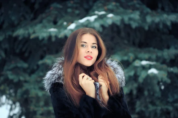 Belle fille souriante sur fond d'arbres enneigés. Portrait d'hiver. manteau avec capuche — Photo