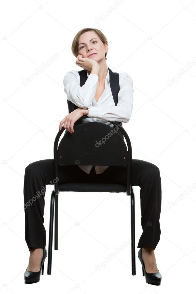 woman sits astride a chair. hand under chin. misses. dominant position. Isolated white background. body language