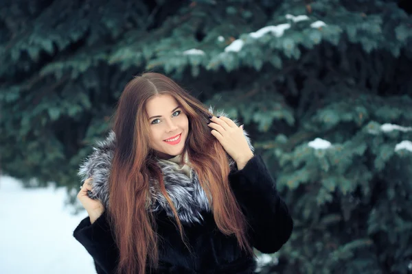 Schöne lächelnde Mädchen auf dem Hintergrund von schneebedeckten Bäumen. Winterporträt. Mantel mit Kapuze — Stockfoto