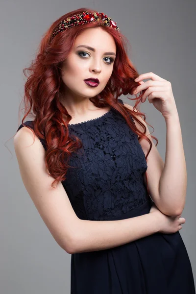 Hermosa modelo de pelo rojo posando en vestido de noche y en la diadema sobre fondo oscuro. gestos femeninos de seducción. lenguaje corporal. tocándose el pelo . — Foto de Stock