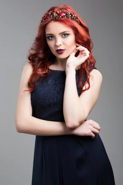 Beautiful red-haired fashion model posing in evening dress and in the diadem over dark background. female gestures of seduction. body language. showing wrist. — Stok fotoğraf