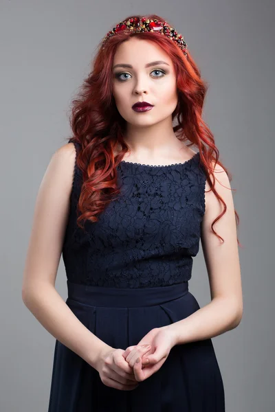 Beautiful red-haired fashion model posing in evening dress and in the diadem over dark background. — Stock Fotó