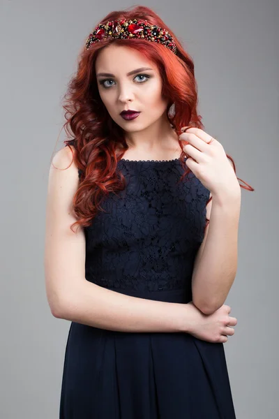 Beautiful red-haired fashion model posing in evening dress and in the diadem over dark background. female gestures of seduction. body language. touching her hair. Wavy Red Hair. Fashion Girl Portrait. — Stockfoto