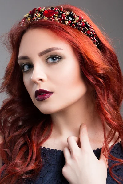 Beautiful red-haired fashion model posing in evening dress and in the diadem over dark background. female gestures of seduction. body language. touching the neck — Stock Photo, Image