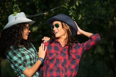 Two attractive girls in cowboy hats and sunglasses walking park. happily laughing