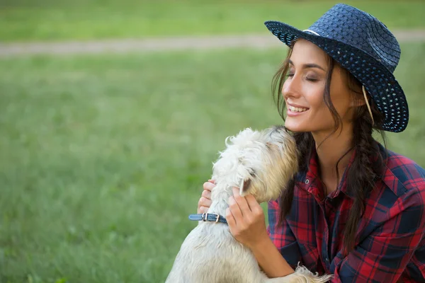 Gadis tersenyum dengan anjing kecilnya. topi koboi dan kemeja kotak-kotak — Stok Foto