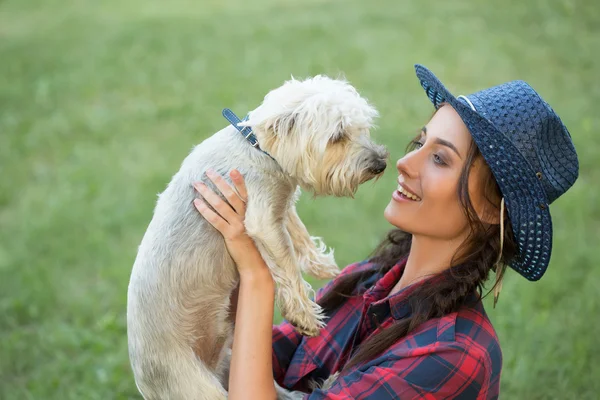 Gadis tersenyum dengan anjing kecilnya. topi koboi dan kemeja kotak-kotak — Stok Foto