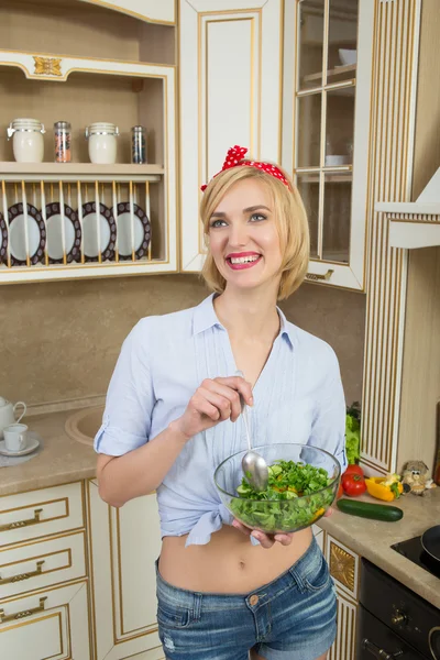 Девушка выглядит позитивно и держит миску с салатом. Он стоит на кухне. — стоковое фото