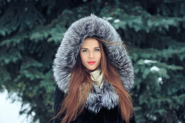 Krásná usměvavá dívka na pozadí zasněžených stromů. Zimní portrét. kabát s kapucí — Stock fotografie