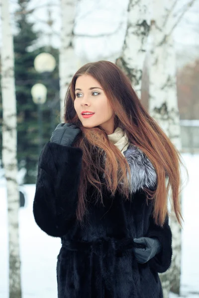 Szép mosolygó lány, háttérben a havas fák. Téli portré. kabát, kapucnival — Stock Fotó